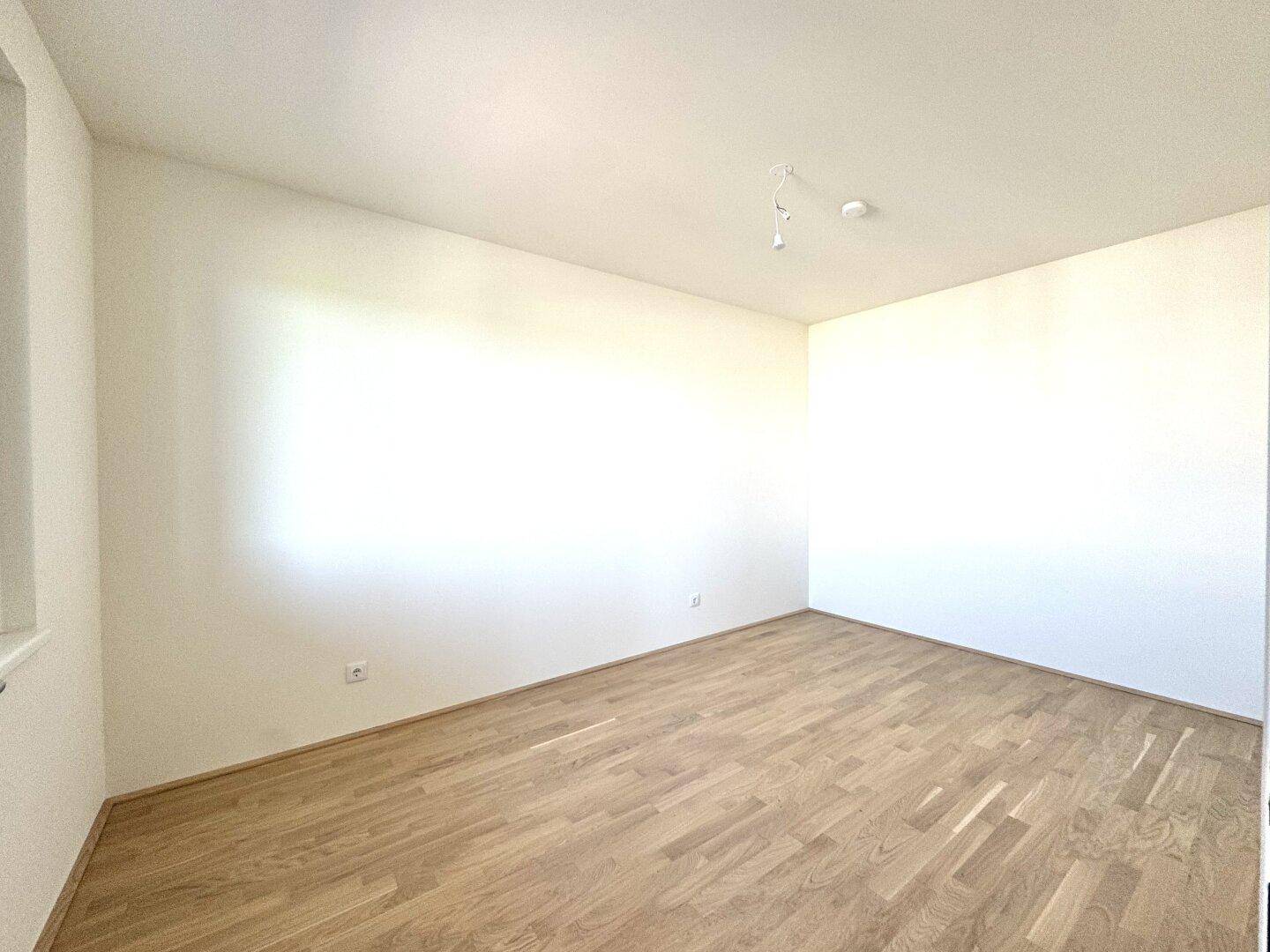 Ruhiges Schlafzimmer mit hellem Parkettboden und viel Tageslicht.