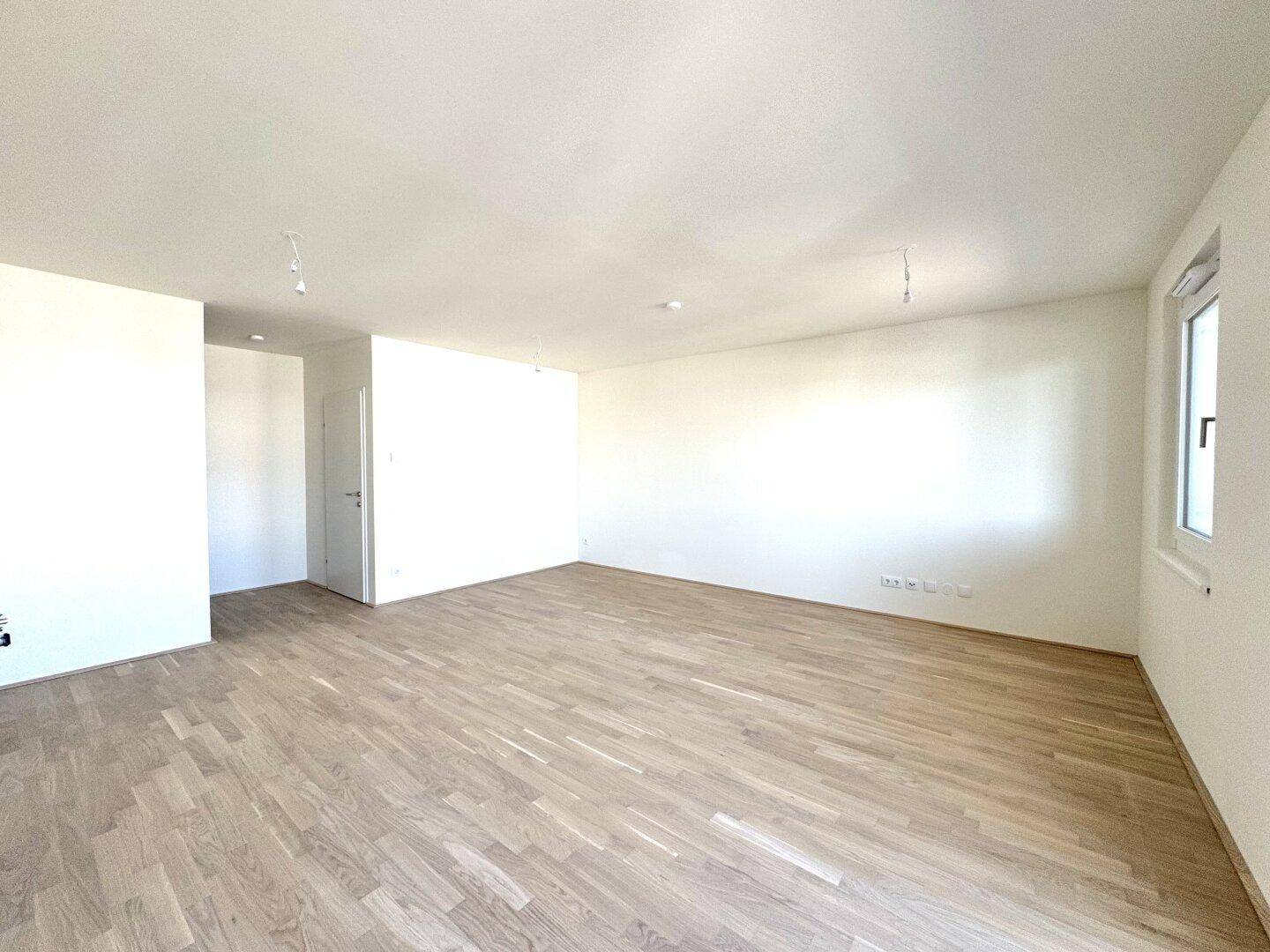 Geräumiger Wohnbereich mit hellem Parkettboden und weiß gestrichenen Wänden.