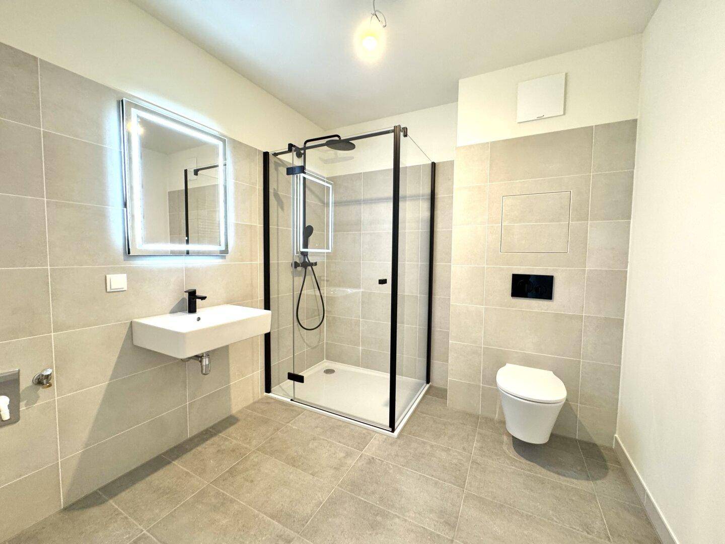 Modernes Badezimmer mit ebenerdiger Dusche, Wand-WC und beleuchtetem Spiegel.