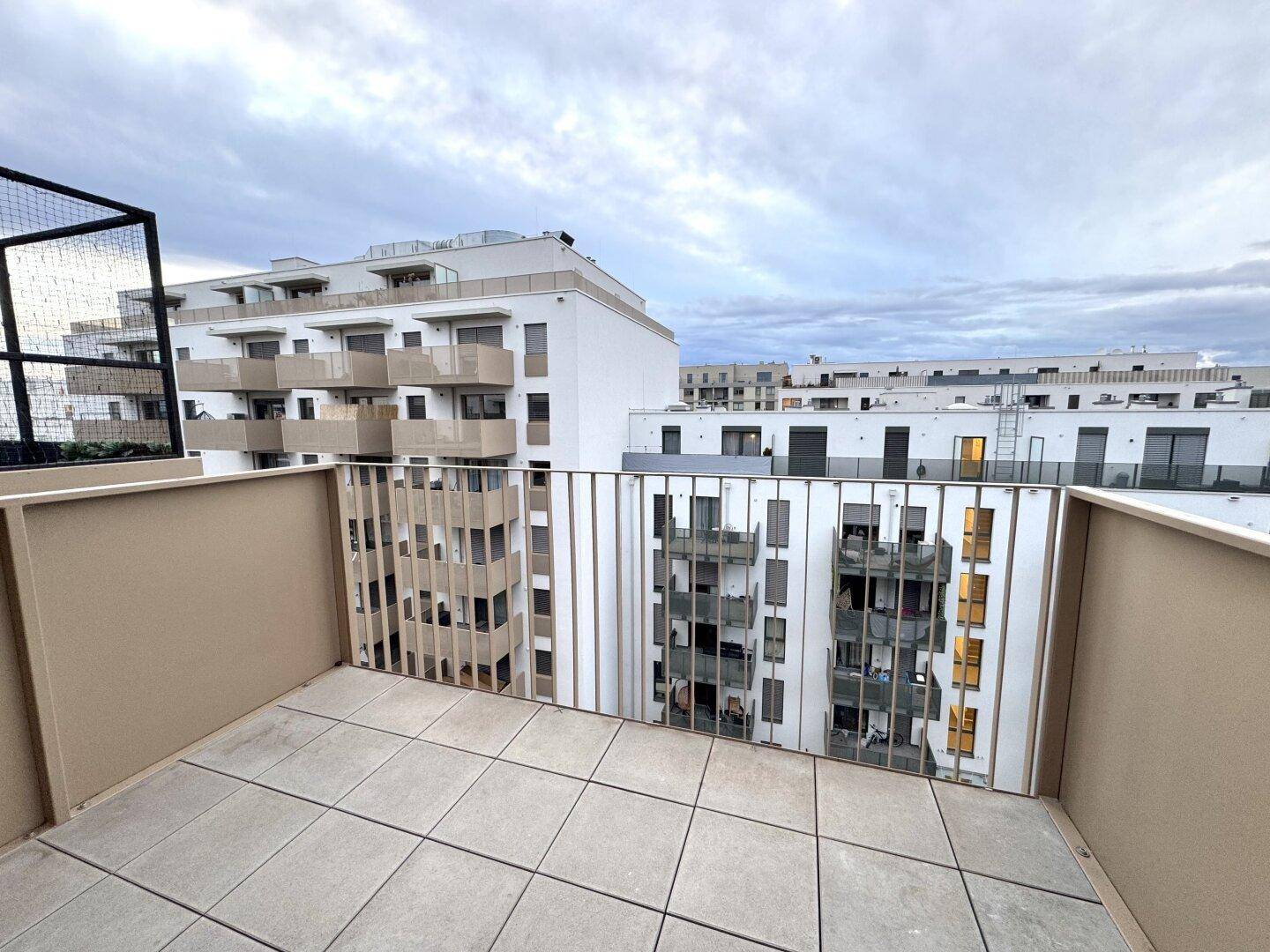 Heller Balkon mit Fliesen und Metallgeländer, bietet einen weiten Blick auf die umliegenden Neubauten.