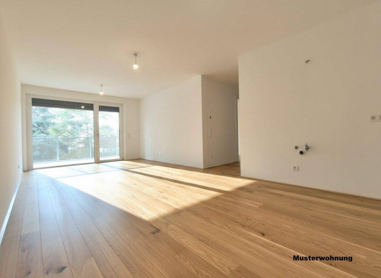 Geräumiges, leeres Wohnzimmer mit Holzboden und großem Schiebefenster zum Balkon in einer Musterwohnung.