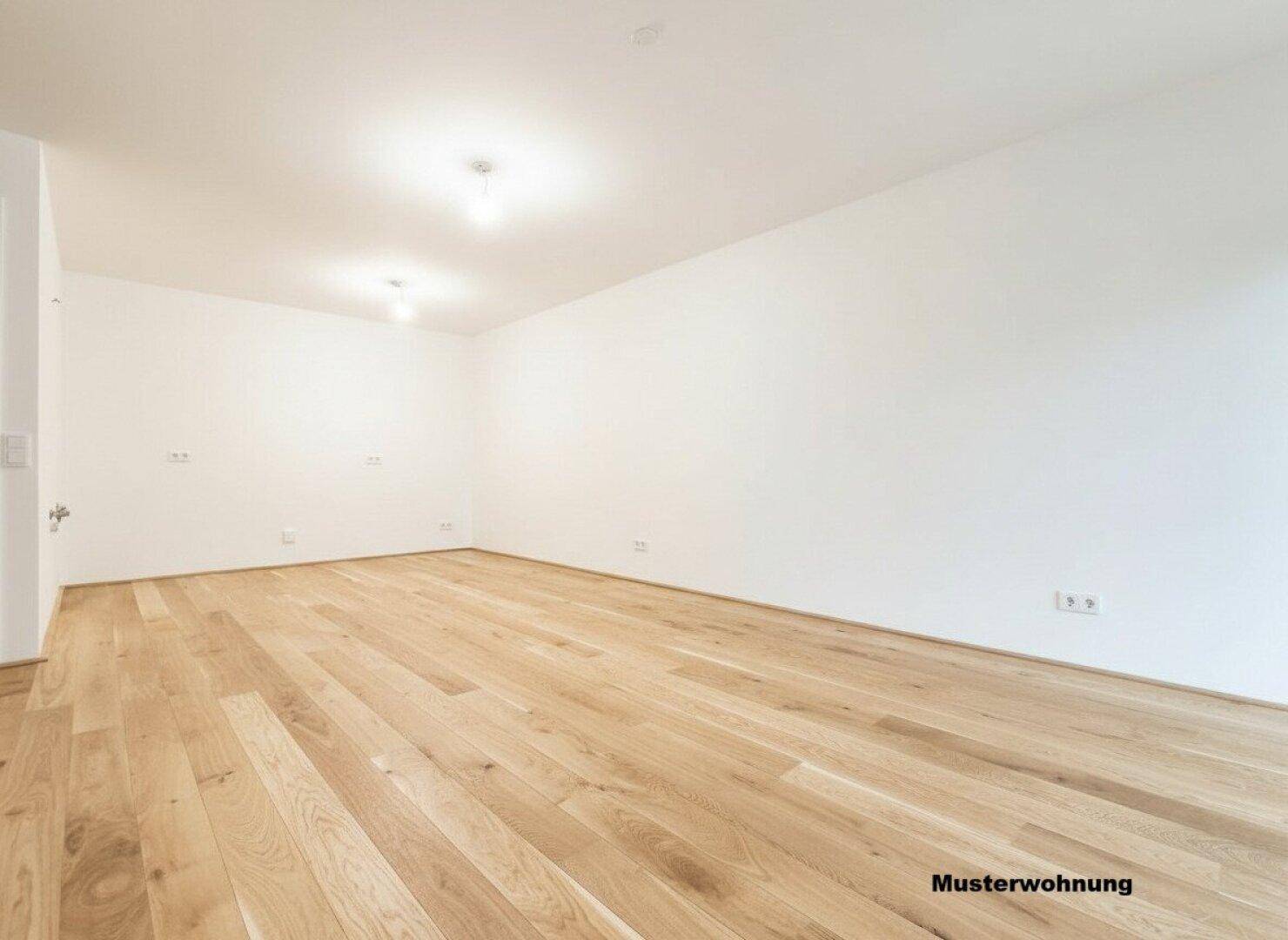 Geräumiger leerer Raum mit hellem Holzboden und weißen Wänden in einer Musterwohnung.