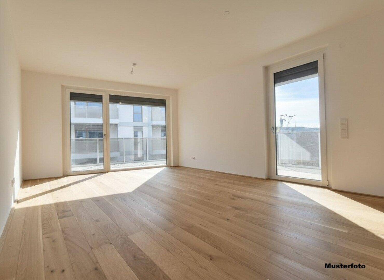 Geräumiger, heller Wohnbereich mit zwei großen Fenstern und Holzboden.
