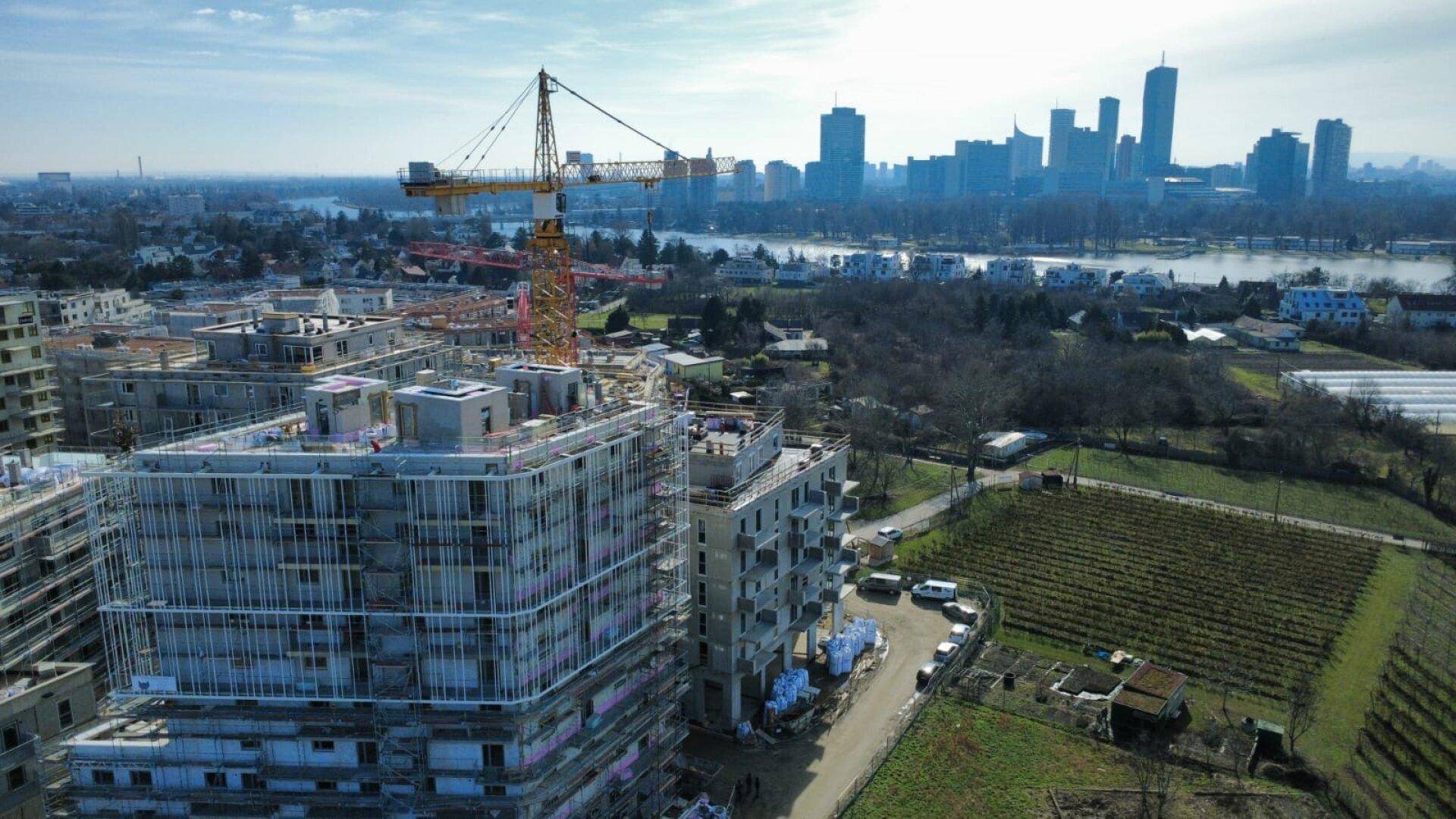Blick von oben auf eine Baustelle mit neuen Wohngebäuden und einem Fluss im Hintergrund.