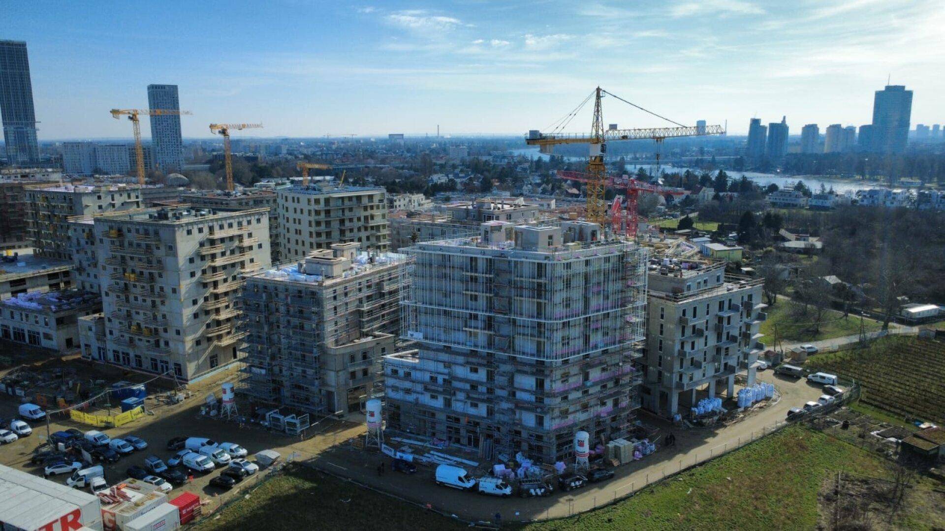 Weitläufige Baustelle mit mehreren im Bau befindlichen Gebäuden und urbaner Skyline im Hintergrund.