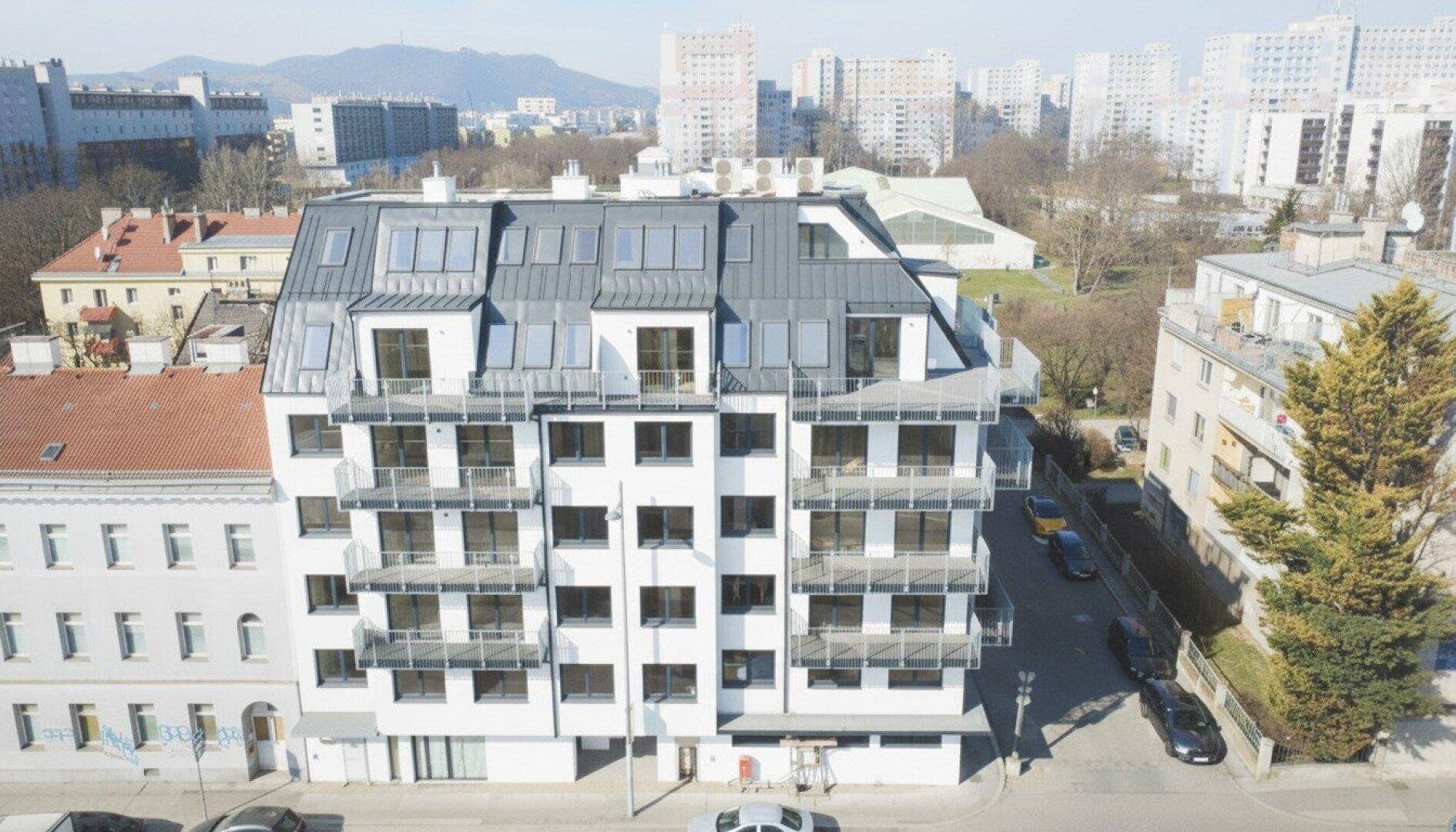 Ansicht eines modernen Mehrfamilienhauses mit Dachgauben und Balkonen in urbaner Lage.