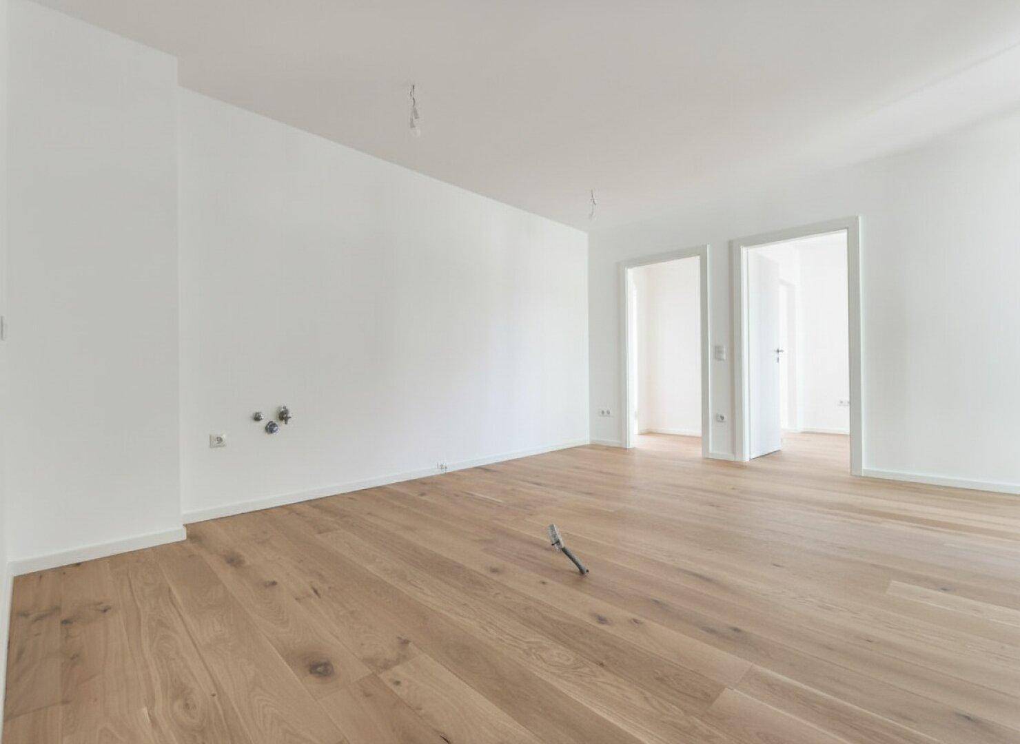 Geräumiges, unmöbliertes Zimmer mit hellem Holzfußboden und weißen Wänden, bereit zum Einzug.