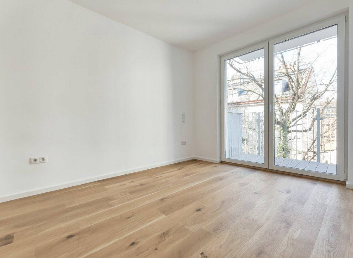 Helles Zimmer mit Holzparkett und großem Fenster, das viel Tageslicht hereinlässt.