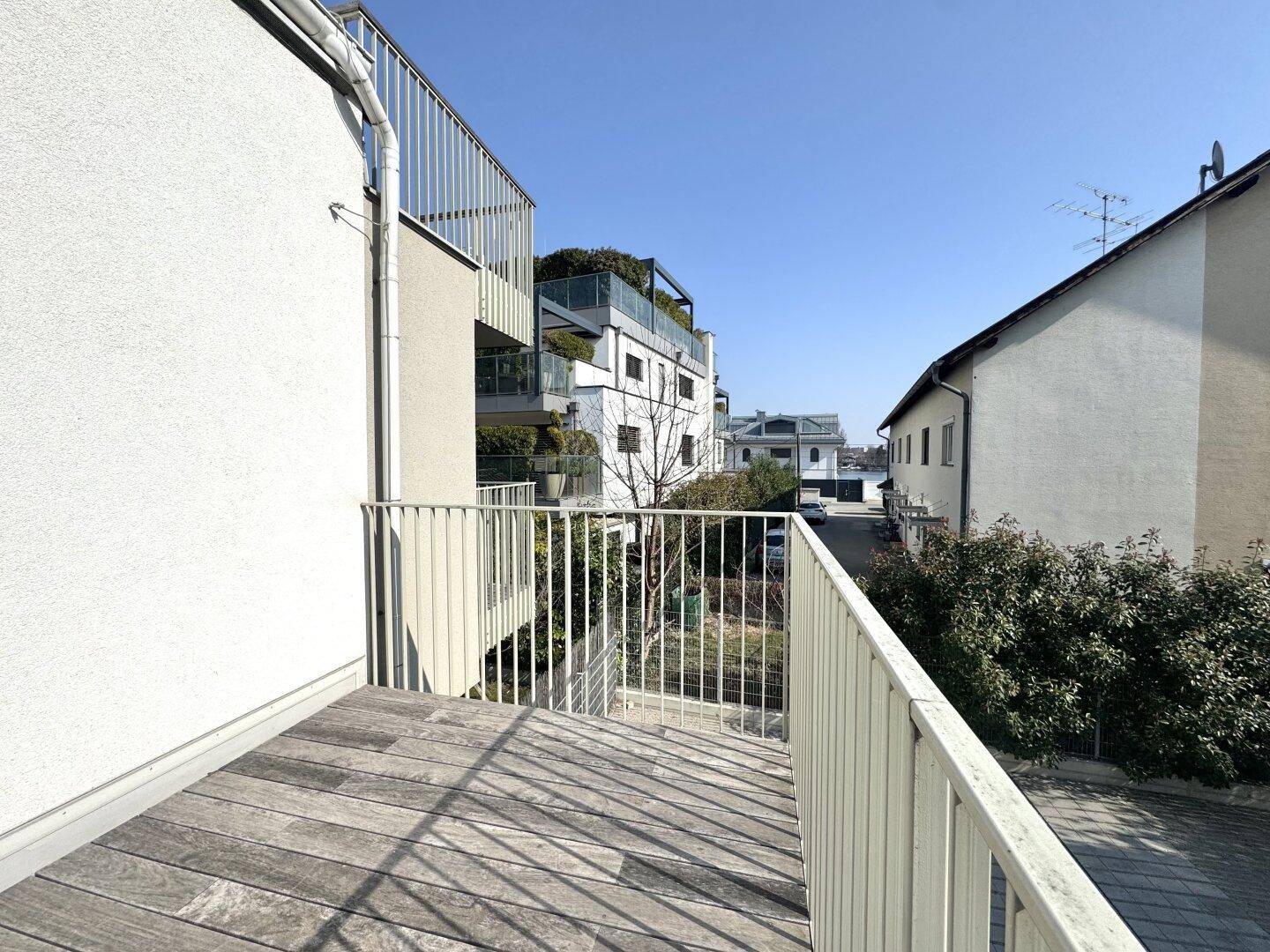 Heller Balkon mit Holzboden und Blick auf die umliegenden modernen Gebäude und Grünflächen.