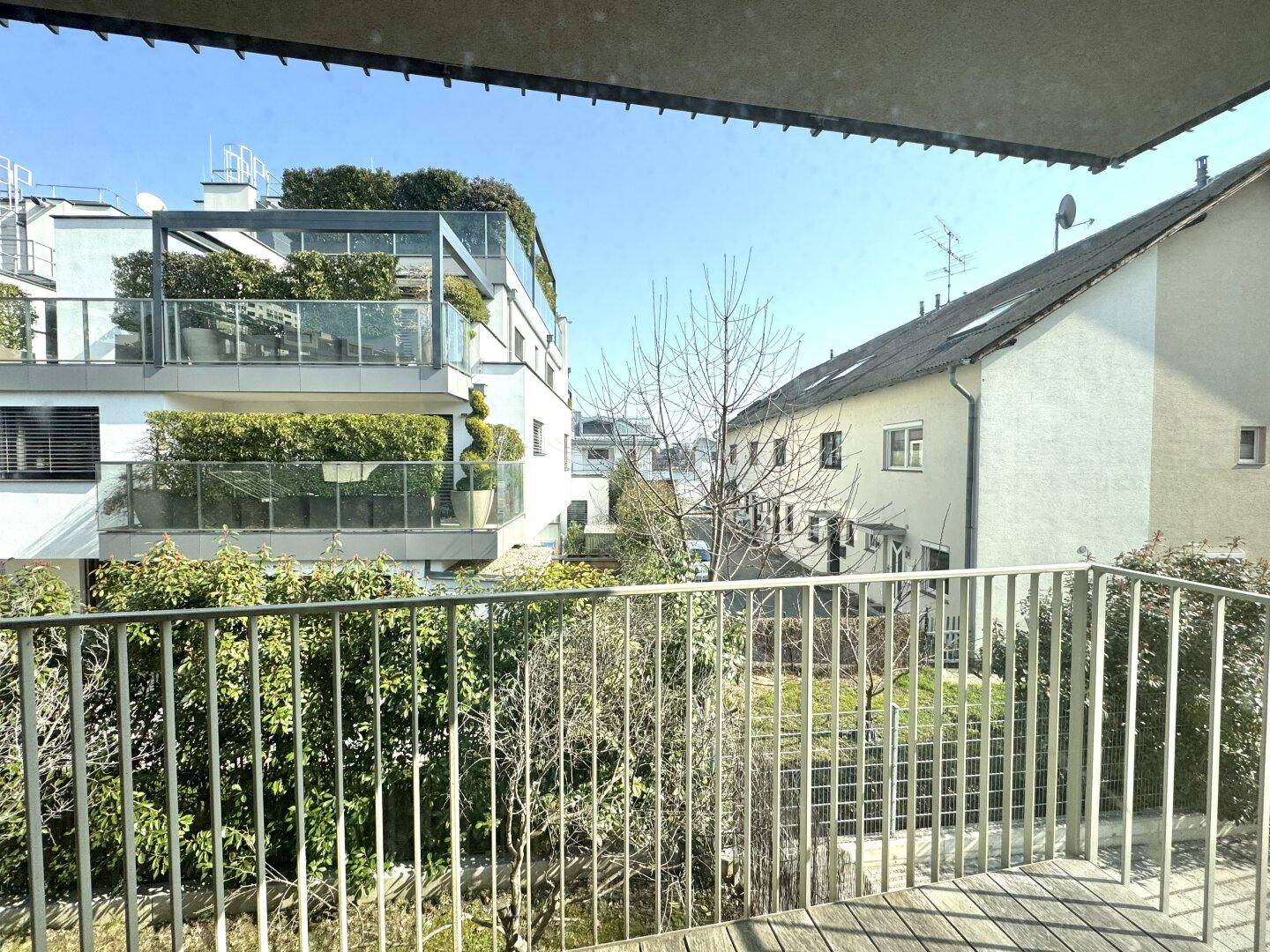 Ausblick vom Balkon auf moderne Gebäude mit begrünten Terrassen und ein traditionelles Nachbarhaus.