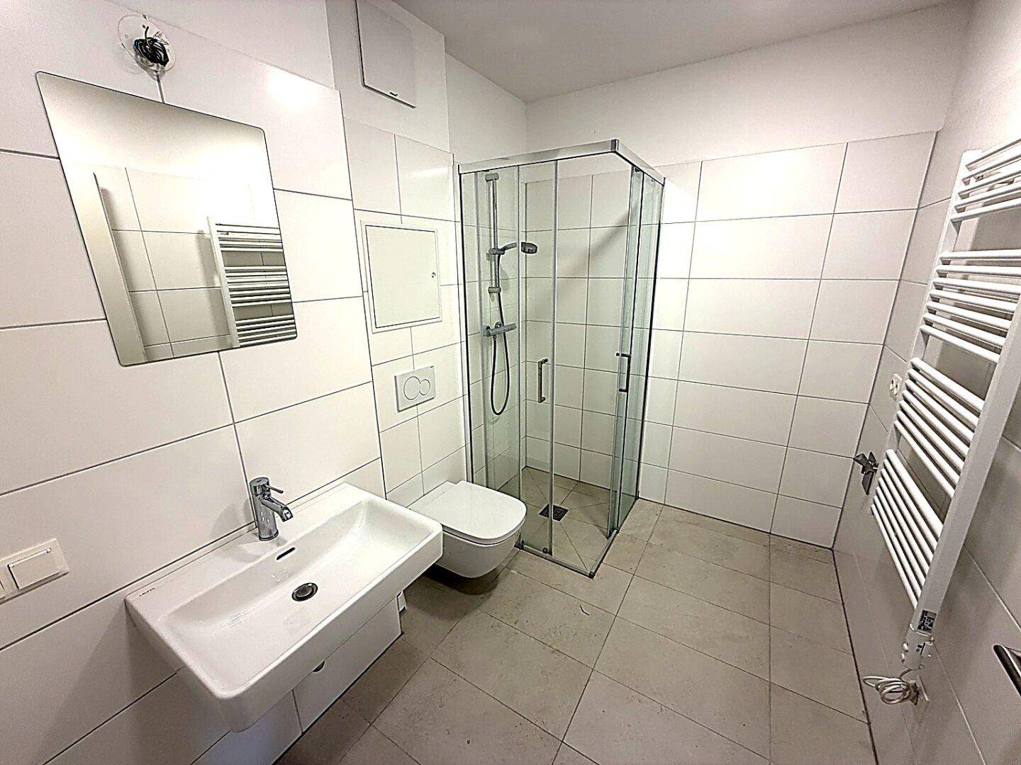 Modernes Badezimmer mit weißen Fliesen, Dusche, WC und beheiztem Handtuchhalter.