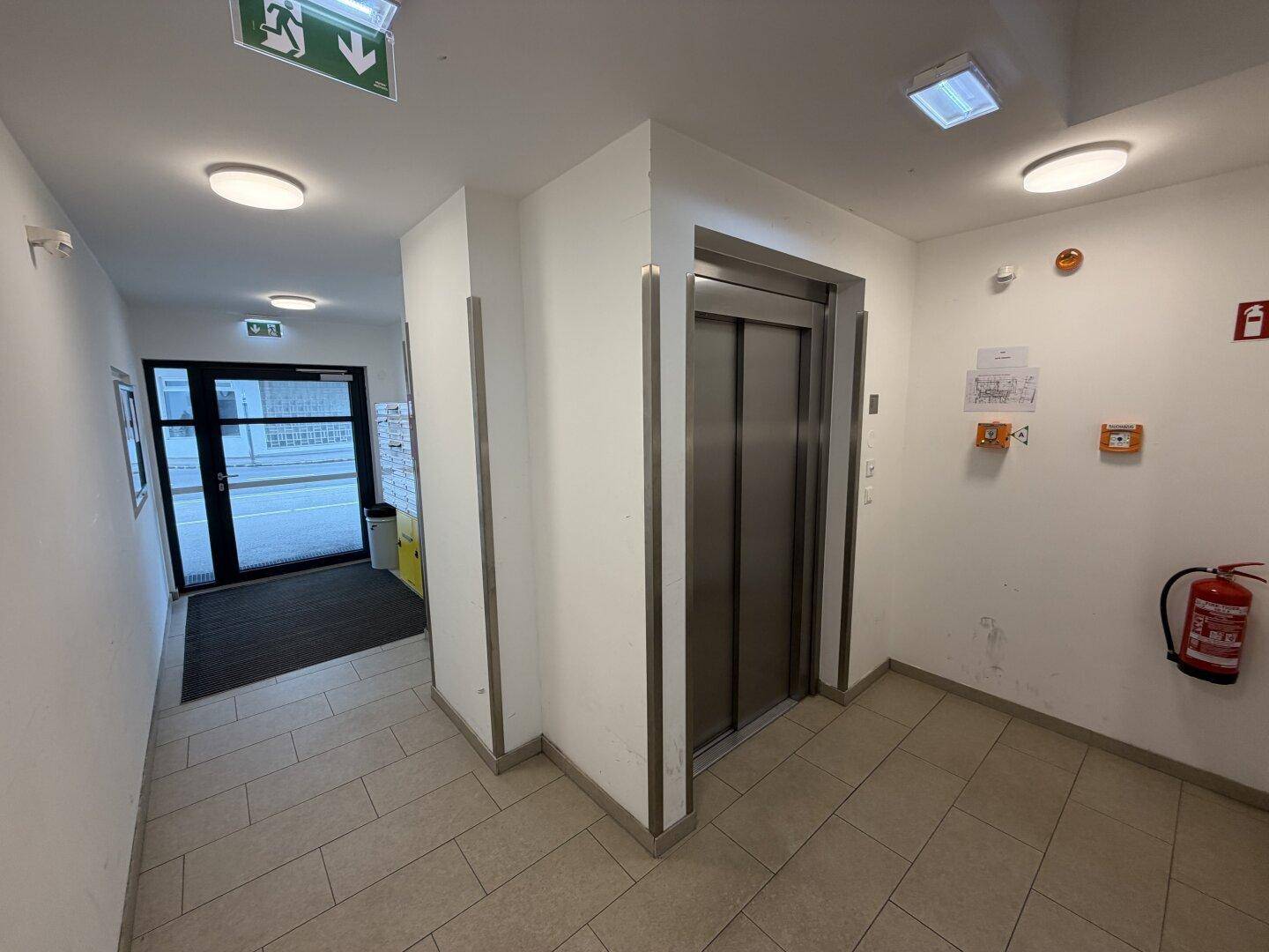 Eingangsbereich des Gebäudes mit Aufzug und Zugang zur Straße, hell gefliest.