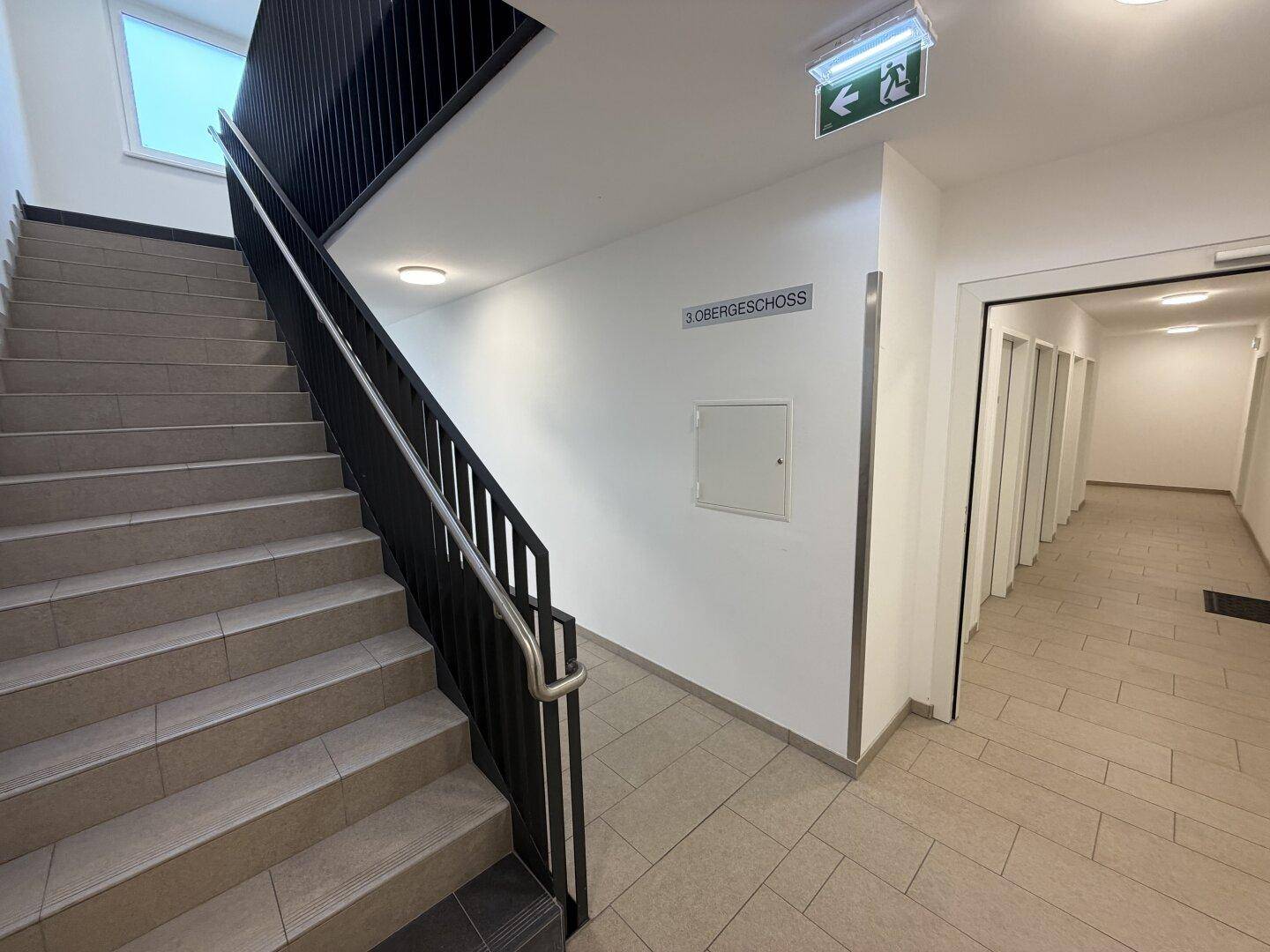 Treppenhaus mit Fliesenstufen und schwarzem Geländer, das zu den oberen Stockwerken führt.