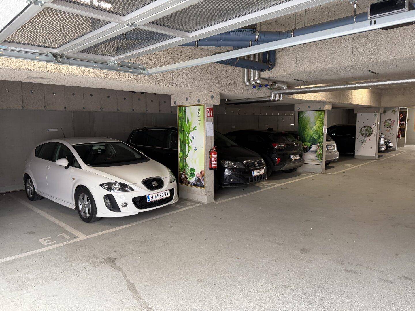Tiefgarage mit mehreren geparkten Autos und sichtbaren Installationen an der Decke.