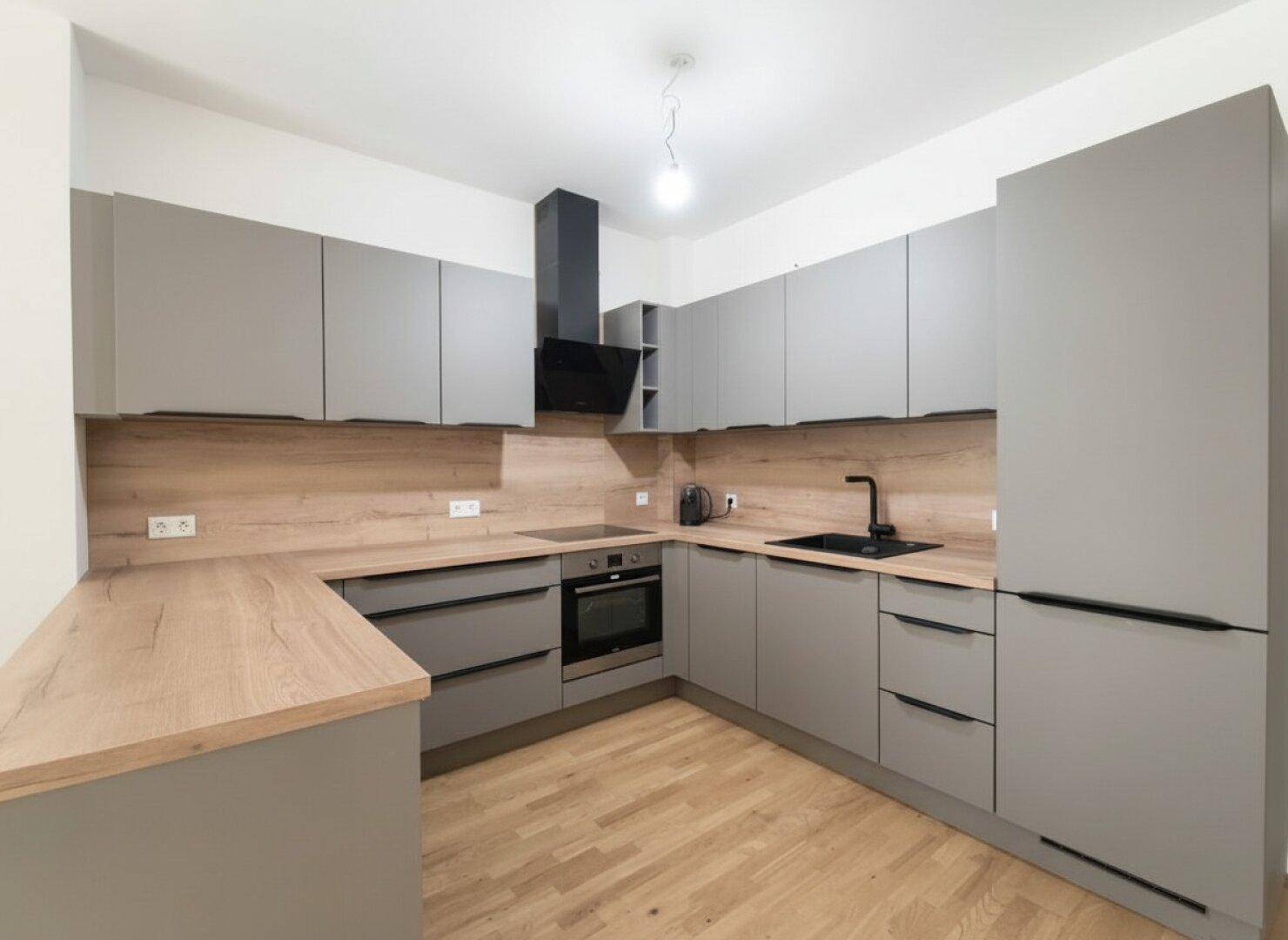 Voll ausgestattete moderne Küche mit grauen Fronten, Holzarbeitsplatten und integriertem Kühlschrank.