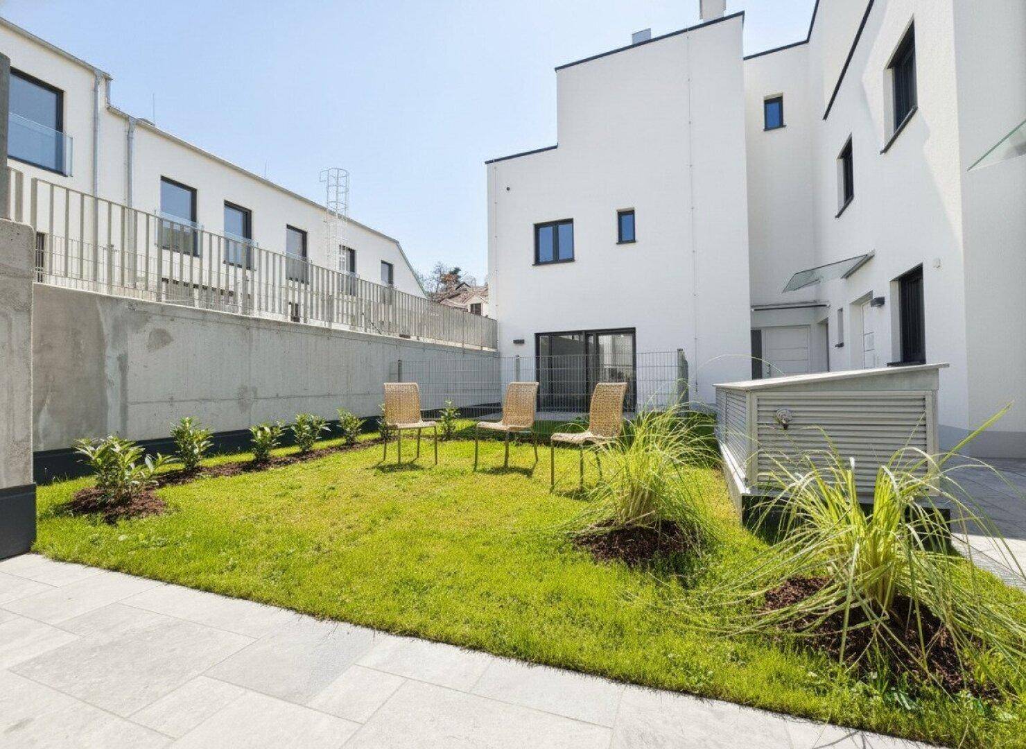 Gepflegter Gartenbereich mit Rasen, jungen Pflanzen und Sitzgelegenheiten im Freien.