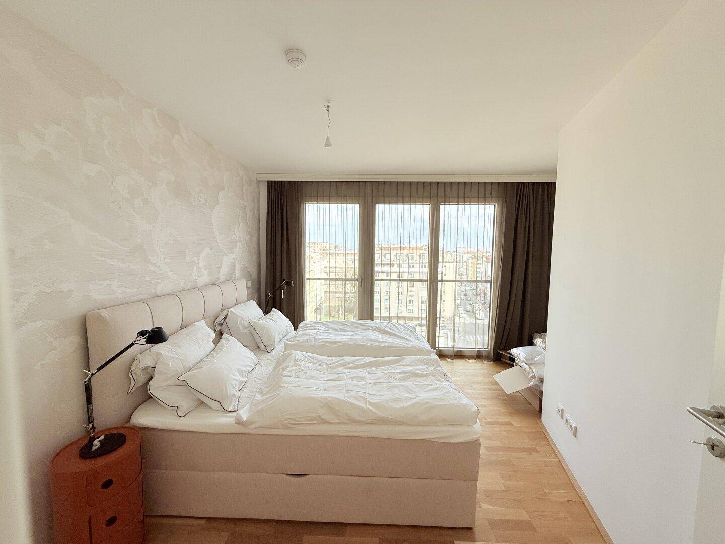 Helles Schlafzimmer mit großem Bett, Parkettboden und Zugang zum Balkon.