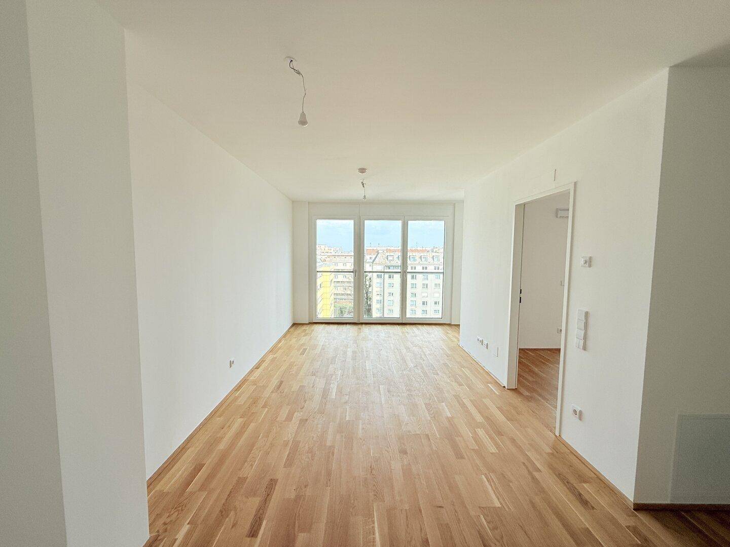 Geräumiges Wohnzimmer mit Parkettboden und großen Fenstern mit Blick auf die Stadt.