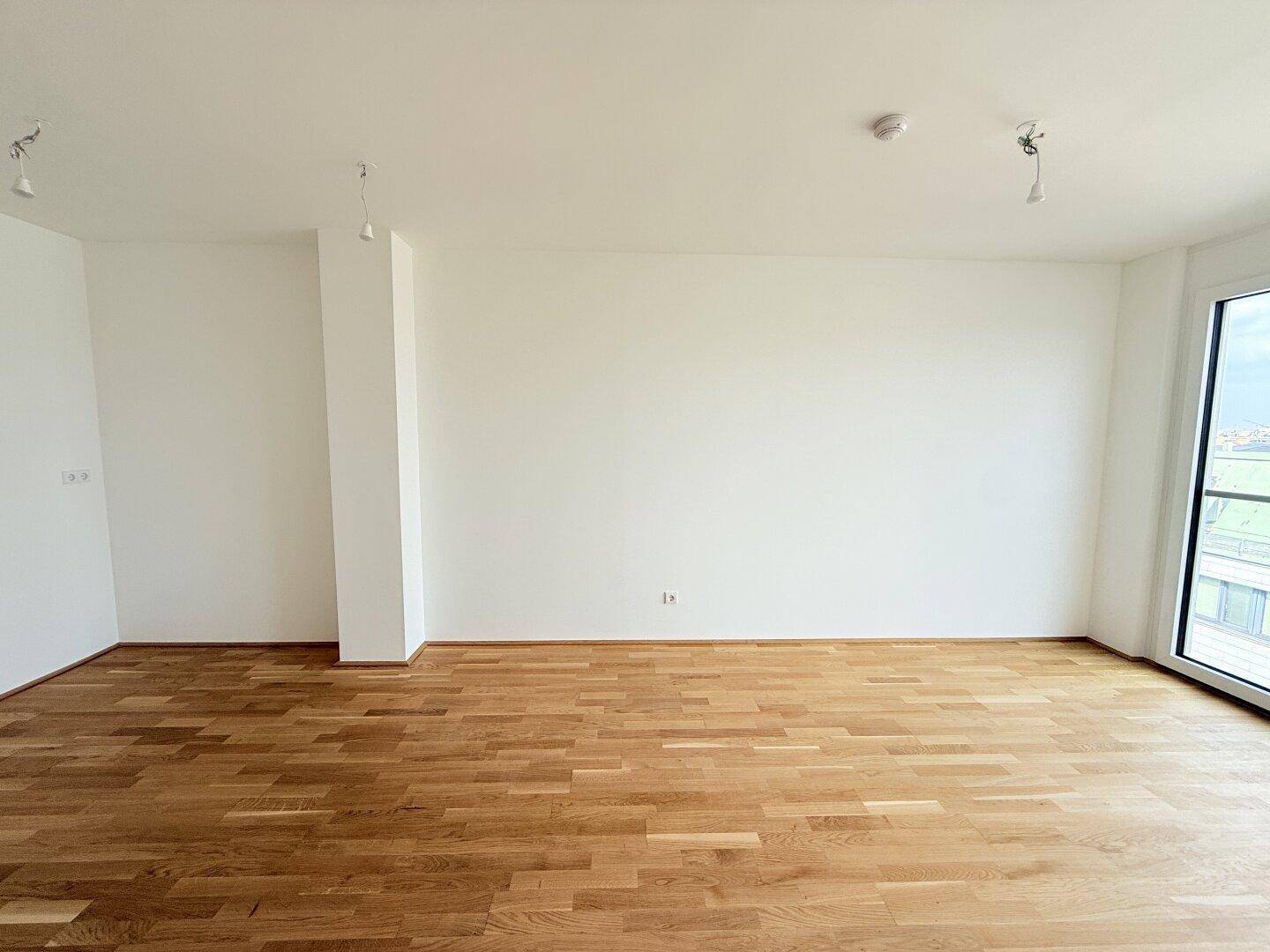 Lichtdurchfluteter Raum mit Parkettboden und Zugang zu einem Außenbereich, bietet viel Tageslicht.
