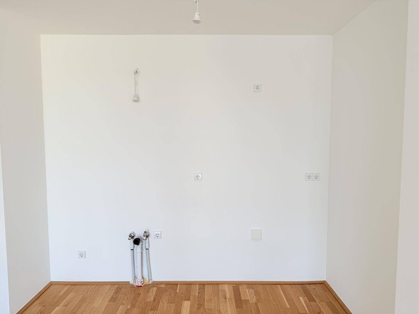 Wandbereich mit Wasseranschlüssen und Steckdosen, vorbereitet für die Kücheninstallation.