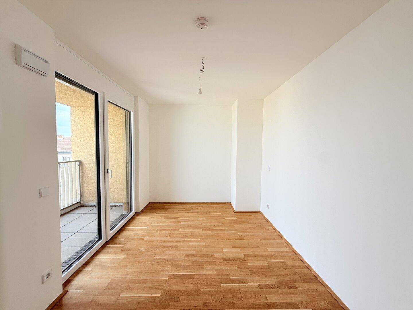 Helles Schlafzimmer mit Parkettboden und großem Fenster, das auf einen Balkon führt.