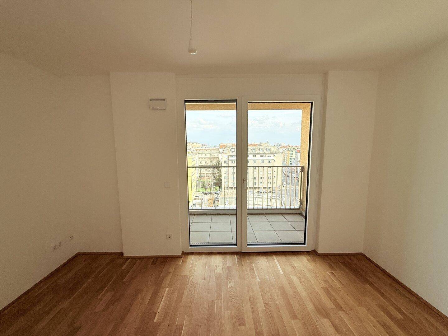 Schlafzimmer mit Parkettboden und Balkonzugang, bietet einen weiten Blick über die Stadt.
