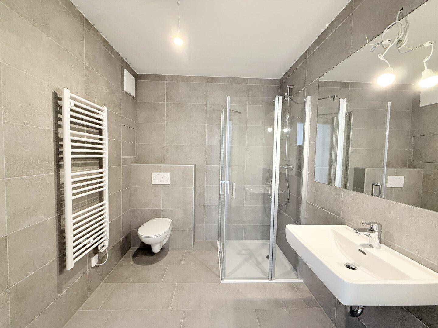 Modernes Badezimmer mit grauen Fliesen, Duschkabine, wandhängendem WC und Handtuchheizkörper.
