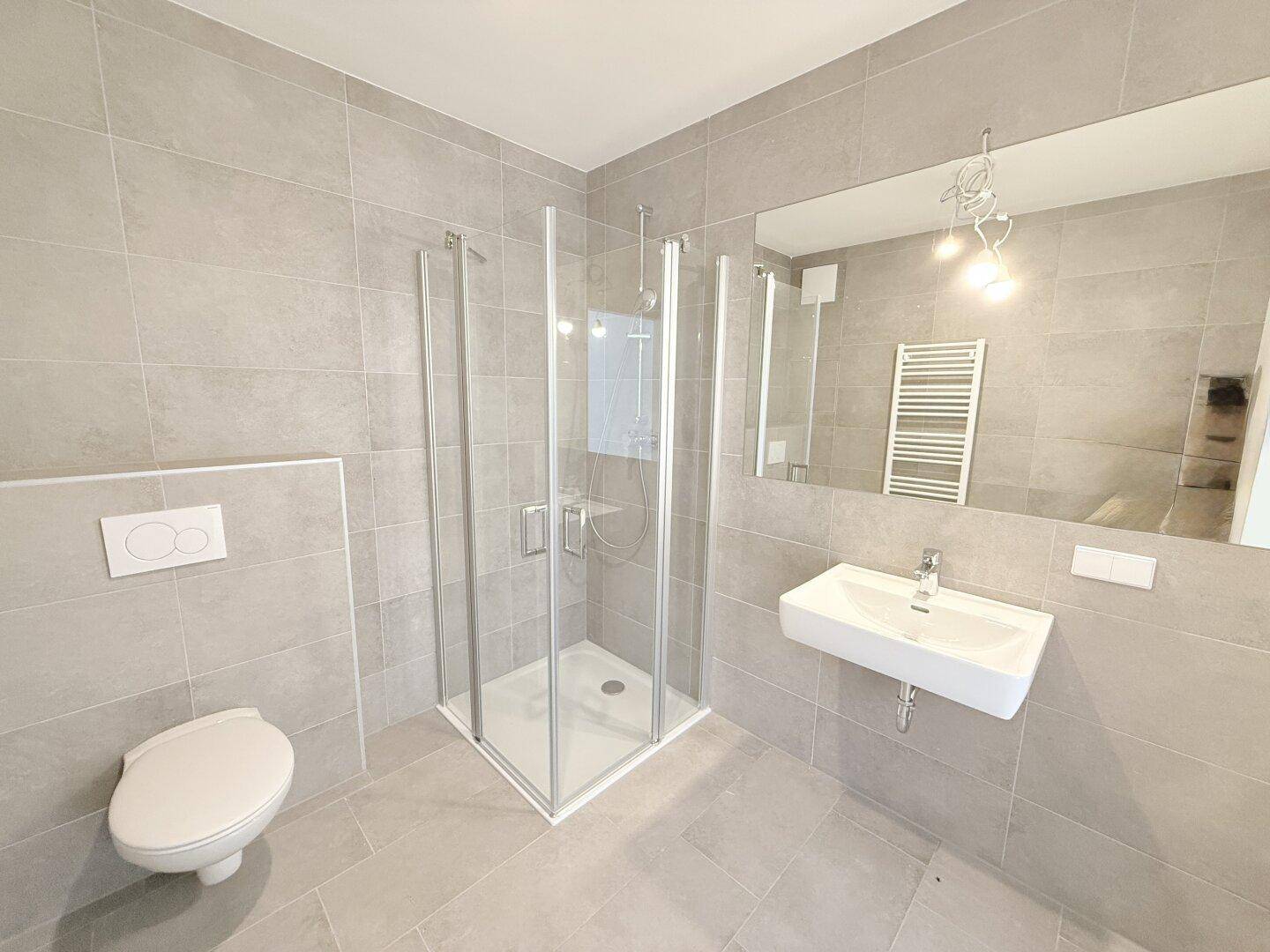 Helles Badezimmer mit modernen grauen Fliesen, Duschkabine und elegantem Waschtisch.