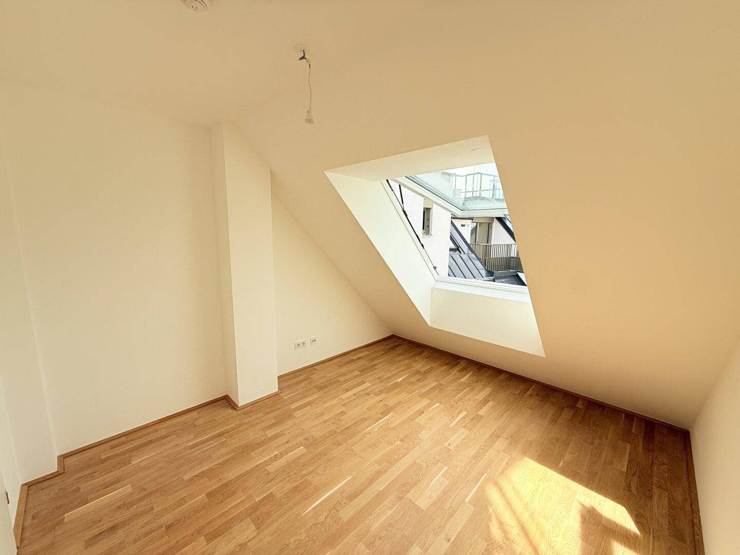 Dachgeschoss-Schlafzimmer mit einem Dachfenster und hellem Parkettboden, bereit zum Einzug.
