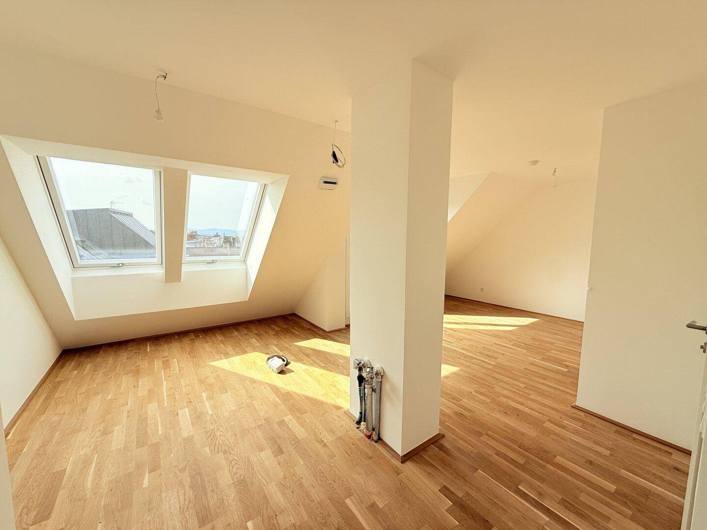 Geräumiges Dachgeschosszimmer mit zwei Dachfenstern und hellem Parkettboden, viel Tageslicht.