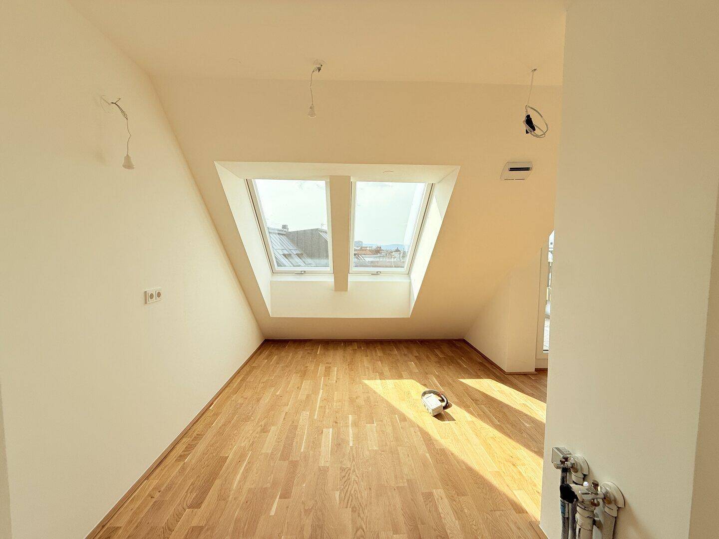 Heller Dachgeschossraum mit zwei großen Dachfenstern und neuem Parkettboden, modern und einladend.