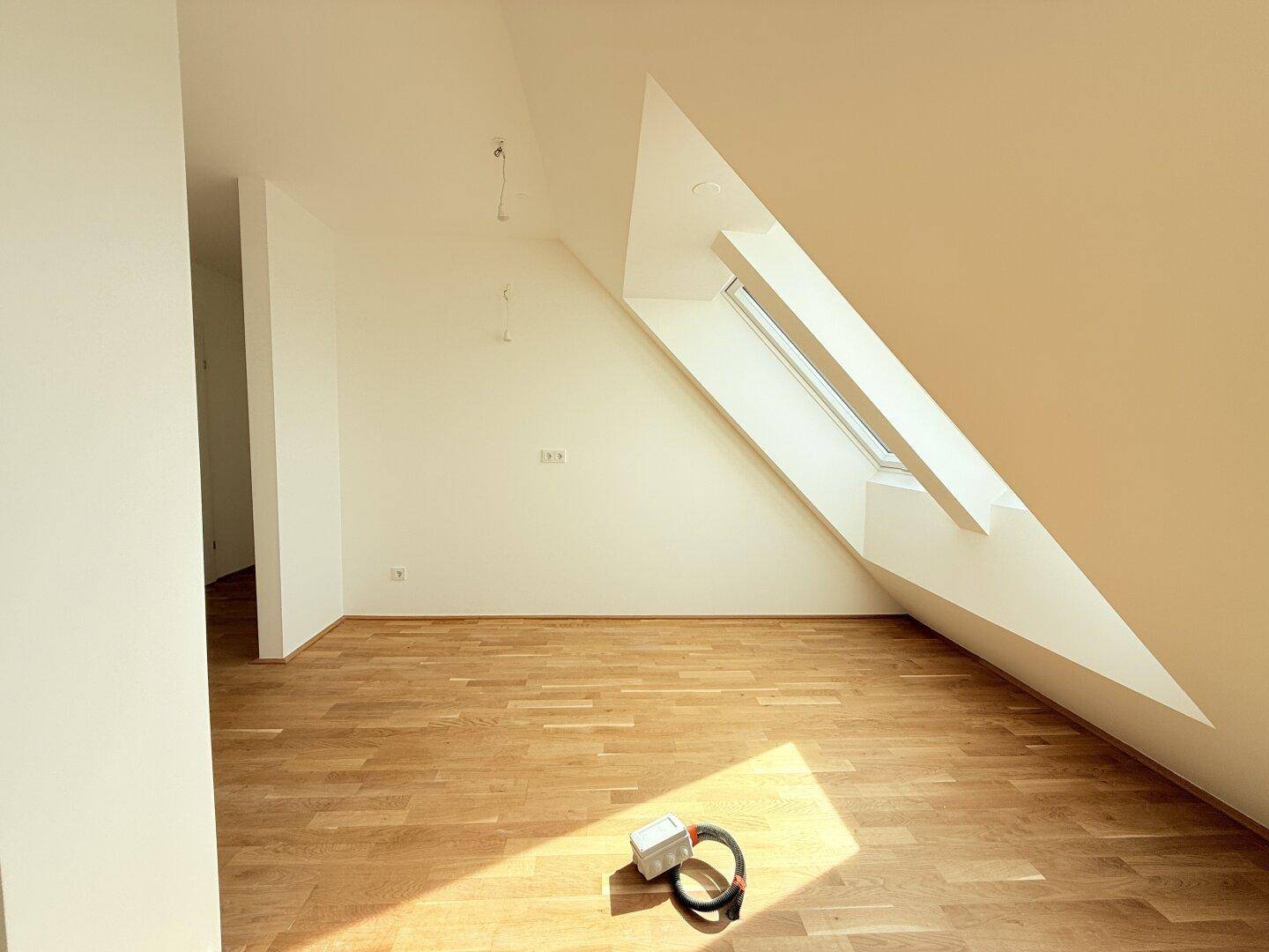 Dachgeschosszimmer mit schrägem Dachfenster und hellem Parkettboden, ideal für ein Büro oder Gästezimmer.