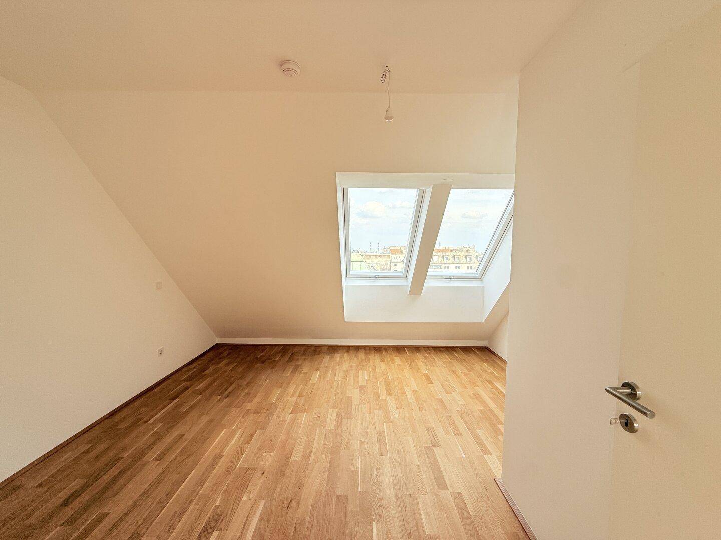 Dachgeschoss-Schlafzimmer mit Parkettboden, schrägen Wänden und viel Tageslicht, einladend und hell.