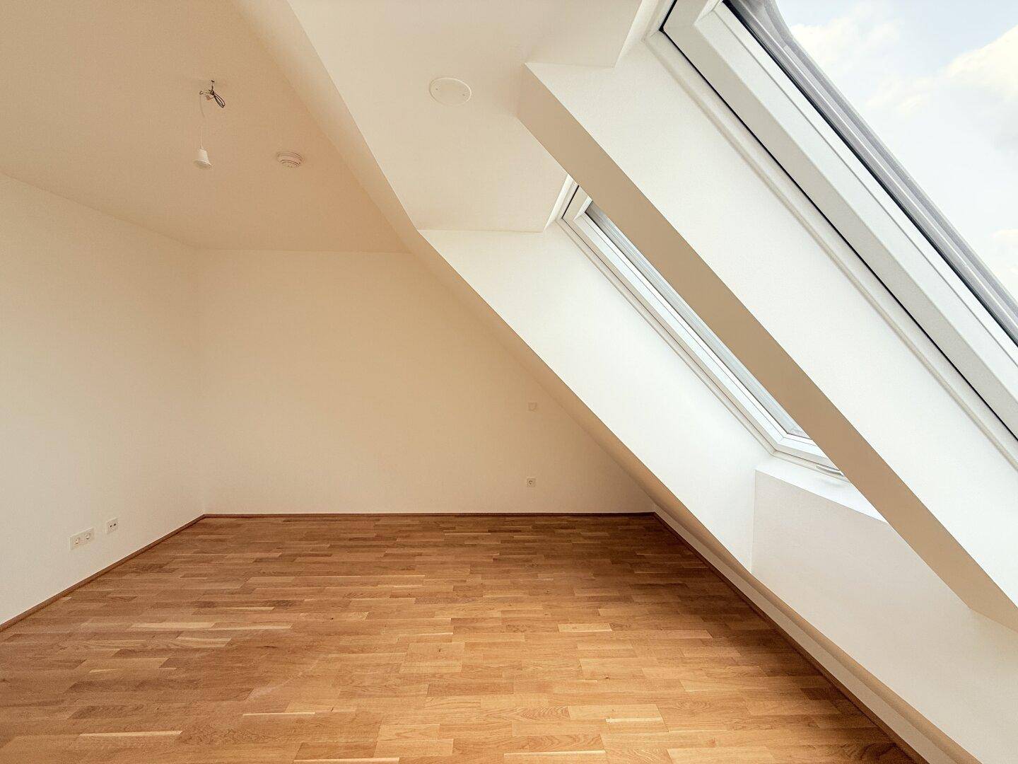 Dachgeschosszimmer mit schrägem Dachfenster und hellem Parkettboden, modern und einladend gestaltet.