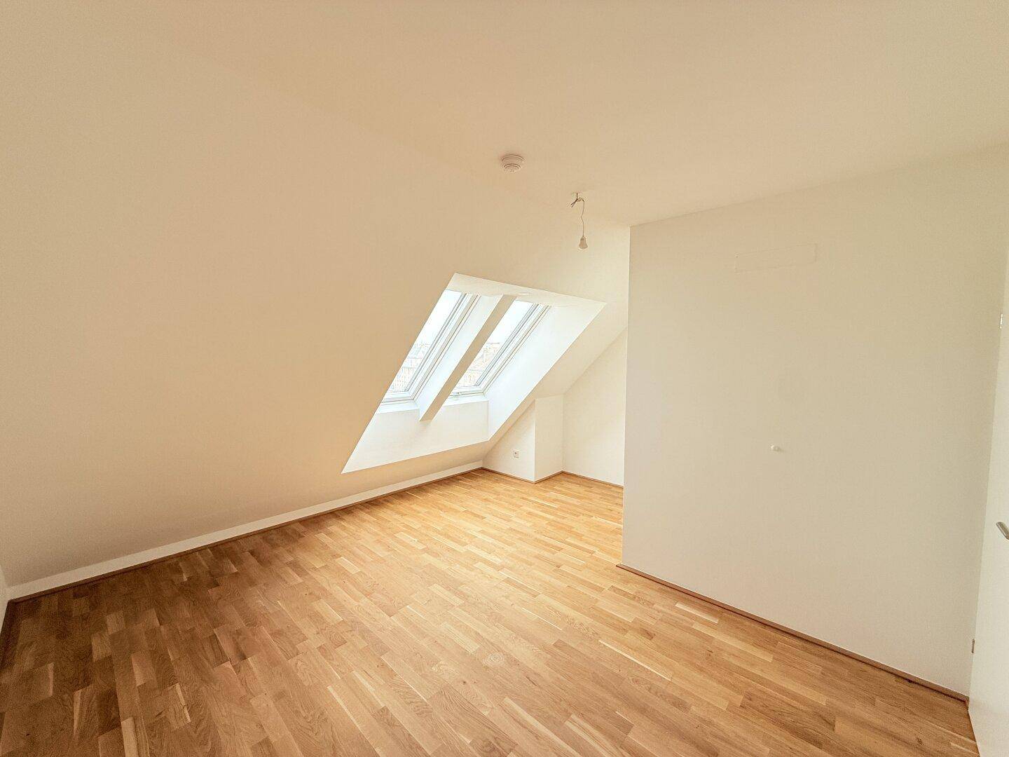 Dachgeschosszimmer mit zwei Dachfenstern und hellem Parkettboden, ideal für ein Kinderzimmer oder Büro.