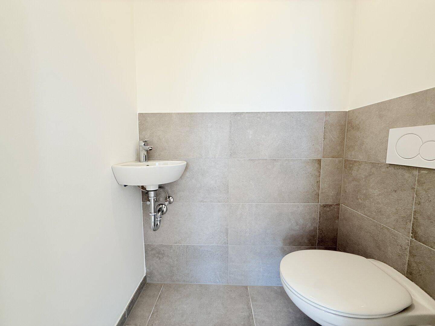 Modernes Gäste-WC mit Wand-WC und kleinem Waschbecken, halbhoch gefliest, sauber und praktisch.