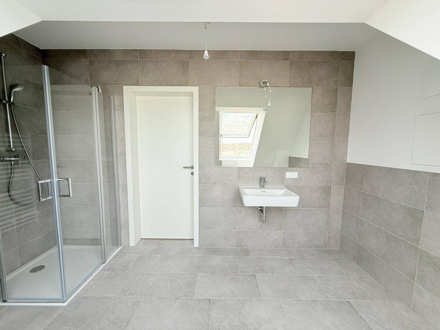 Helles Badezimmer mit Dusche, Waschbecken und großem Spiegel im Dachgeschoss, modern und funktional.