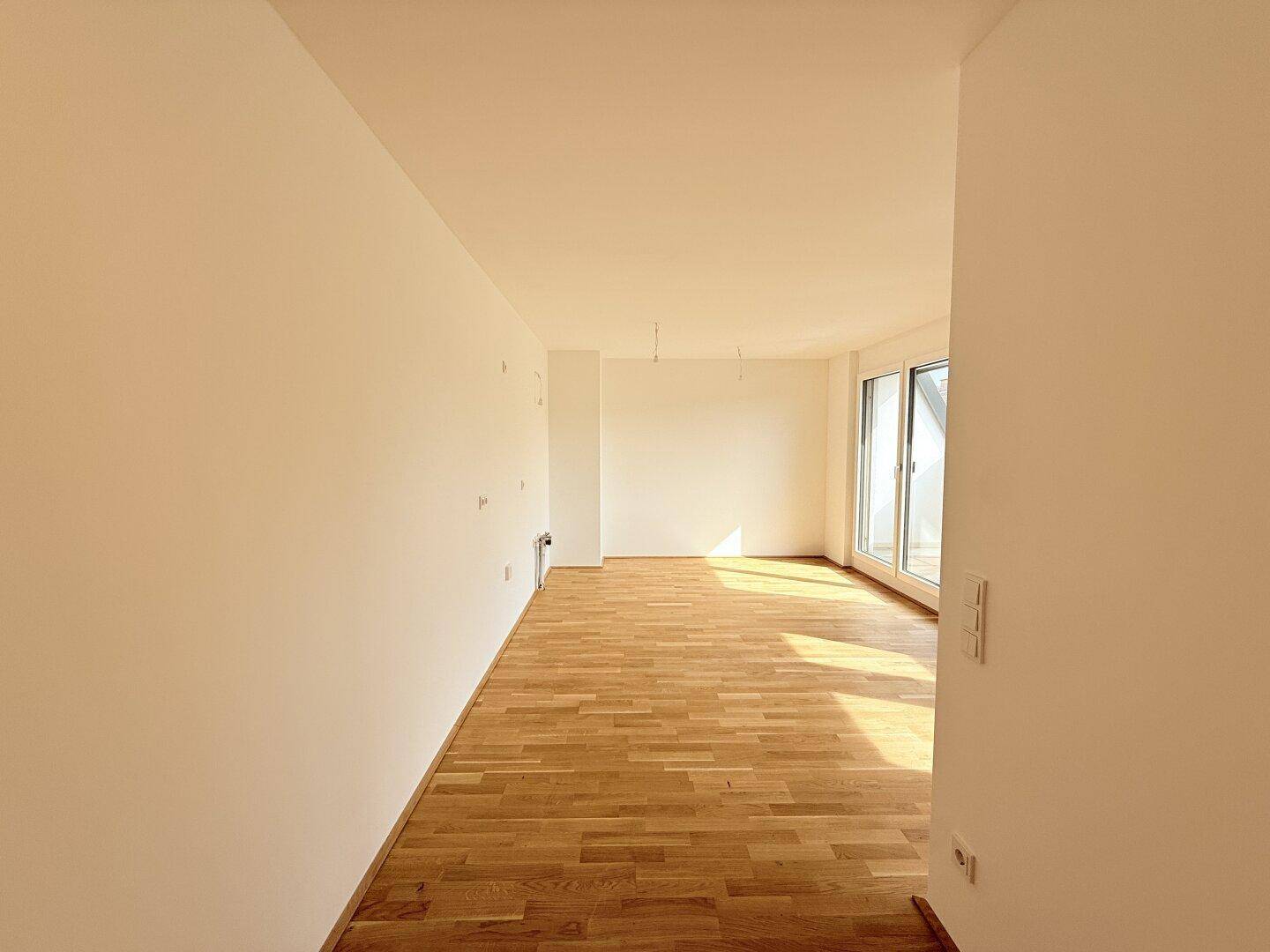 Langer, heller Wohnraum mit Parkettboden und großem Fenster, das Zugang zum Balkon bietet.