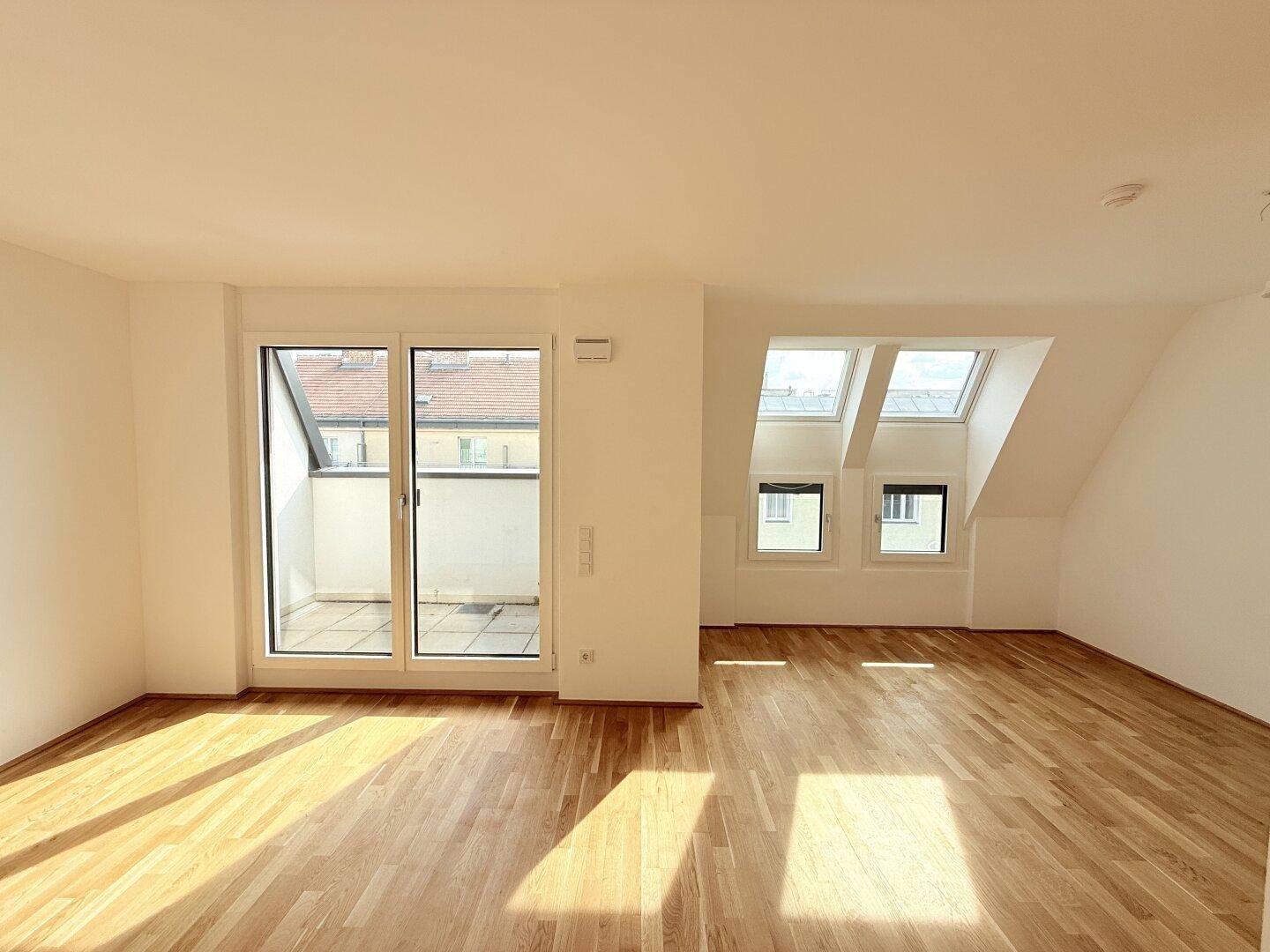 Lichtdurchfluteter Raum im Dachgeschoss mit Parkettboden, Dachfenstern und Zugang zum Balkon.