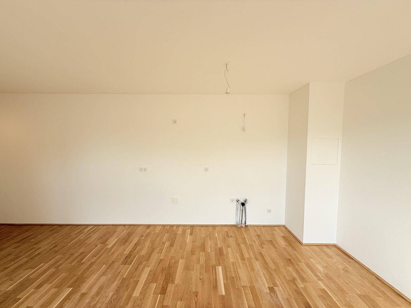 Leerer Raum mit Parkettboden, weißen Wänden und sichtbaren Elektroinstallationen für zukünftige Anschlüsse.