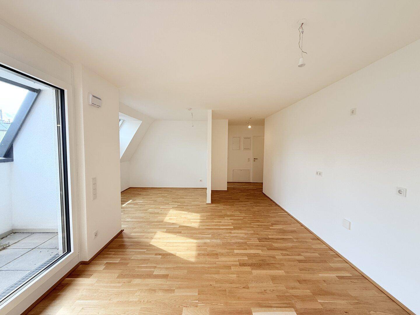 Geräumiger, heller Wohnbereich mit Parkettboden, Balkonzugang und Blick in den Flur.