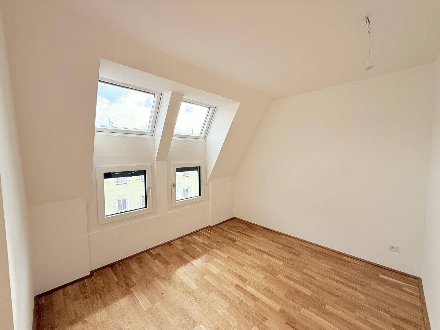 Dachgeschosszimmer mit Parkettboden, schrägen Wänden und zwei großen Dachfenstern, die viel Licht spenden.