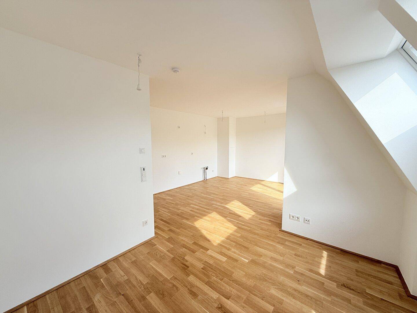 Offener Wohnbereich mit Parkettboden, hellen Wänden und einem Übergang zu einem Zimmer mit Dachschräge.