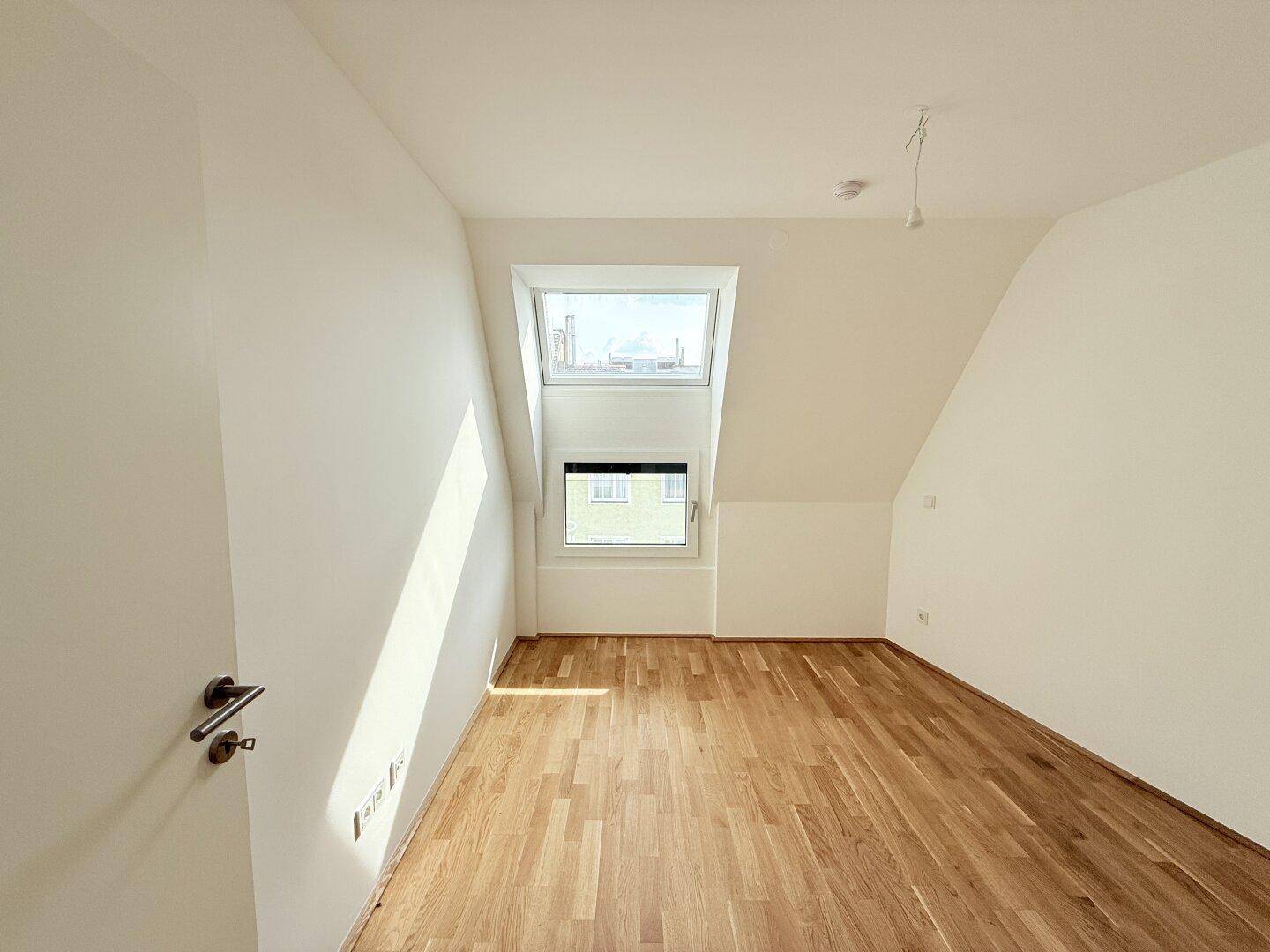 Helles Schlafzimmer mit Parkettboden, Dachschräge und einem großen Fenster für natürliche Belichtung.