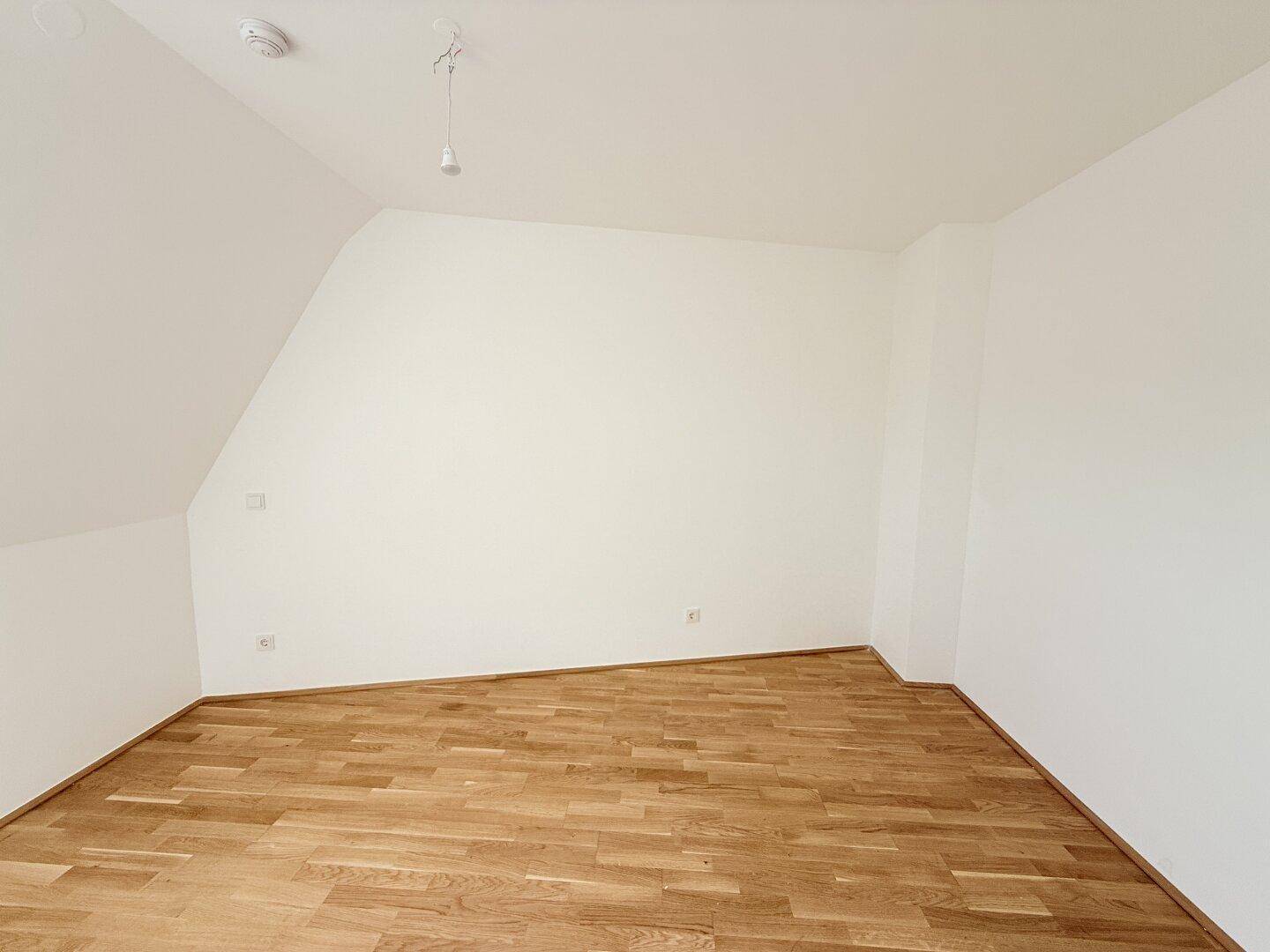 Geräumiges Zimmer mit Parkettboden und schrägen Wänden, bereit für individuelle Einrichtung.