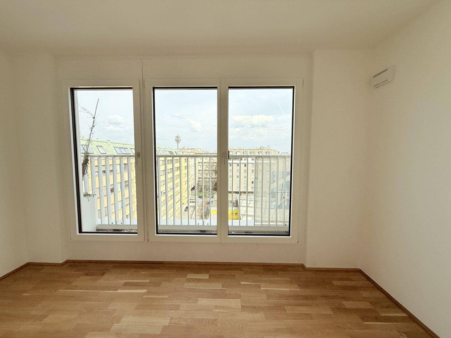 Helles Zimmer mit Parkettboden und Fenstern, die einen Blick auf die Stadt bieten.