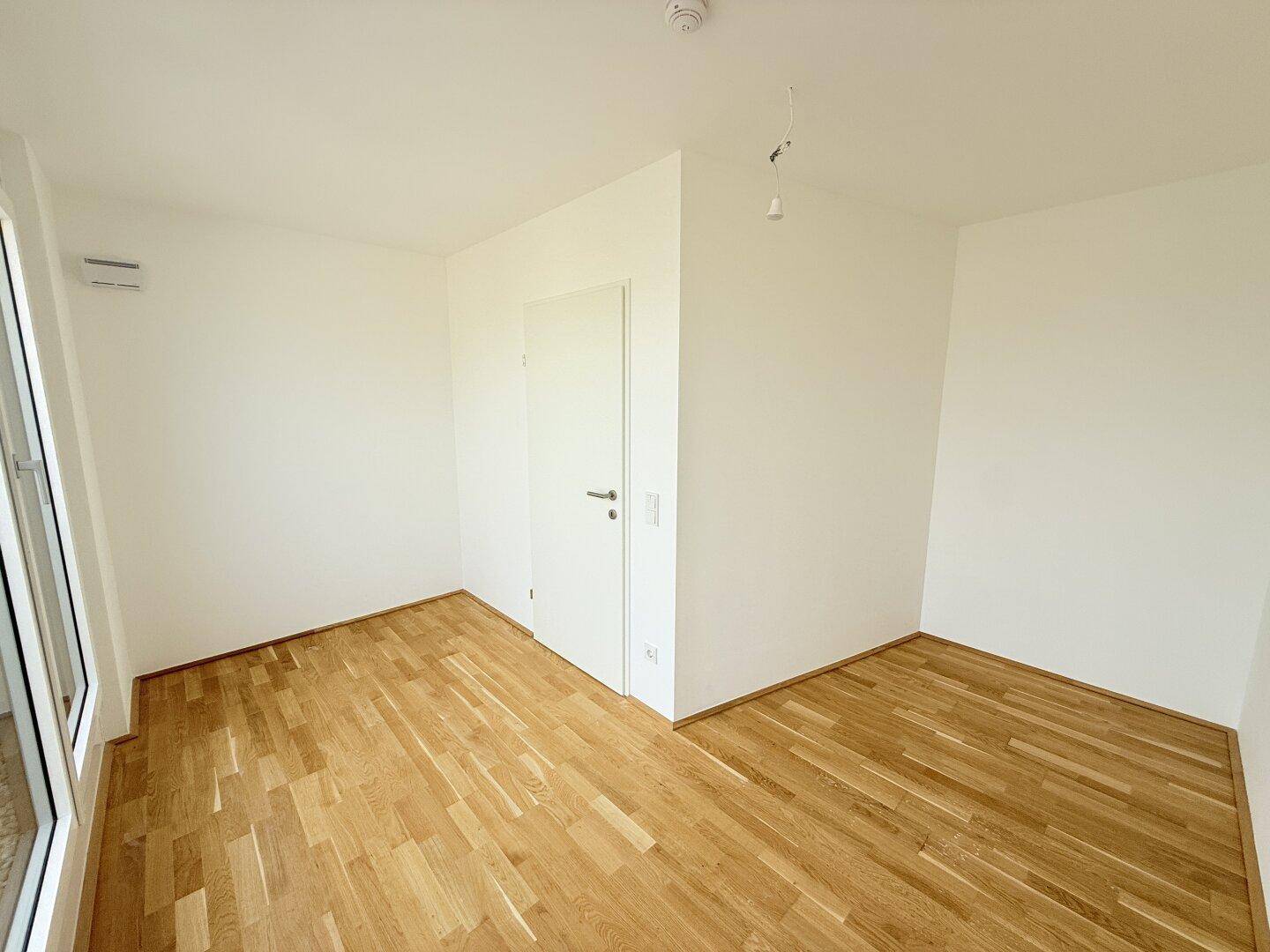 Leeres Schlafzimmer mit Parkettboden und weiß gestrichenen Wänden, bereit zur Einrichtung.