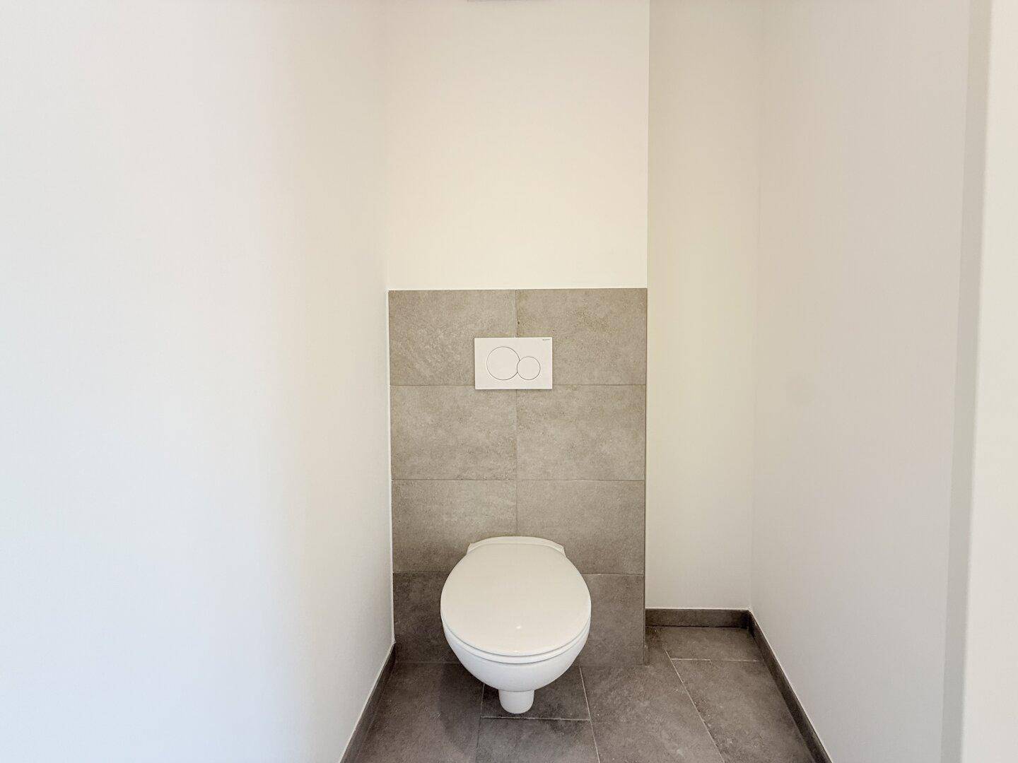 Sauberes Gäste-WC mit Wand-WC und modernen grauen Fliesen an Wänden und Boden.