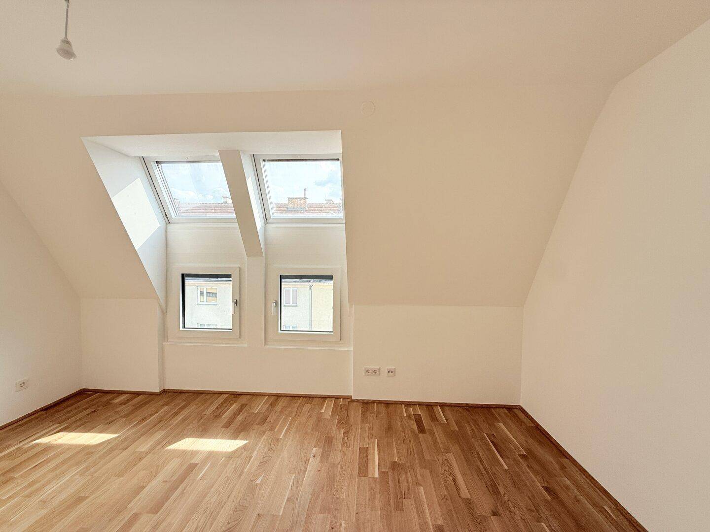 Geräumiges Dachzimmer mit Parkettboden, schrägen Wänden und mehreren Dachfenstern.