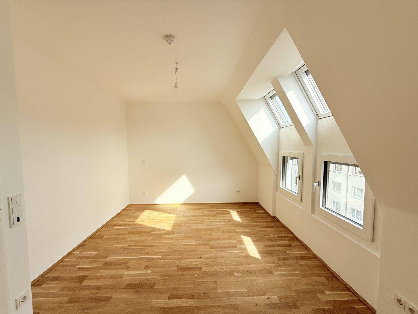 Helles Dachzimmer mit Parkettboden und schrägen Wänden, die viel Charakter verleihen.